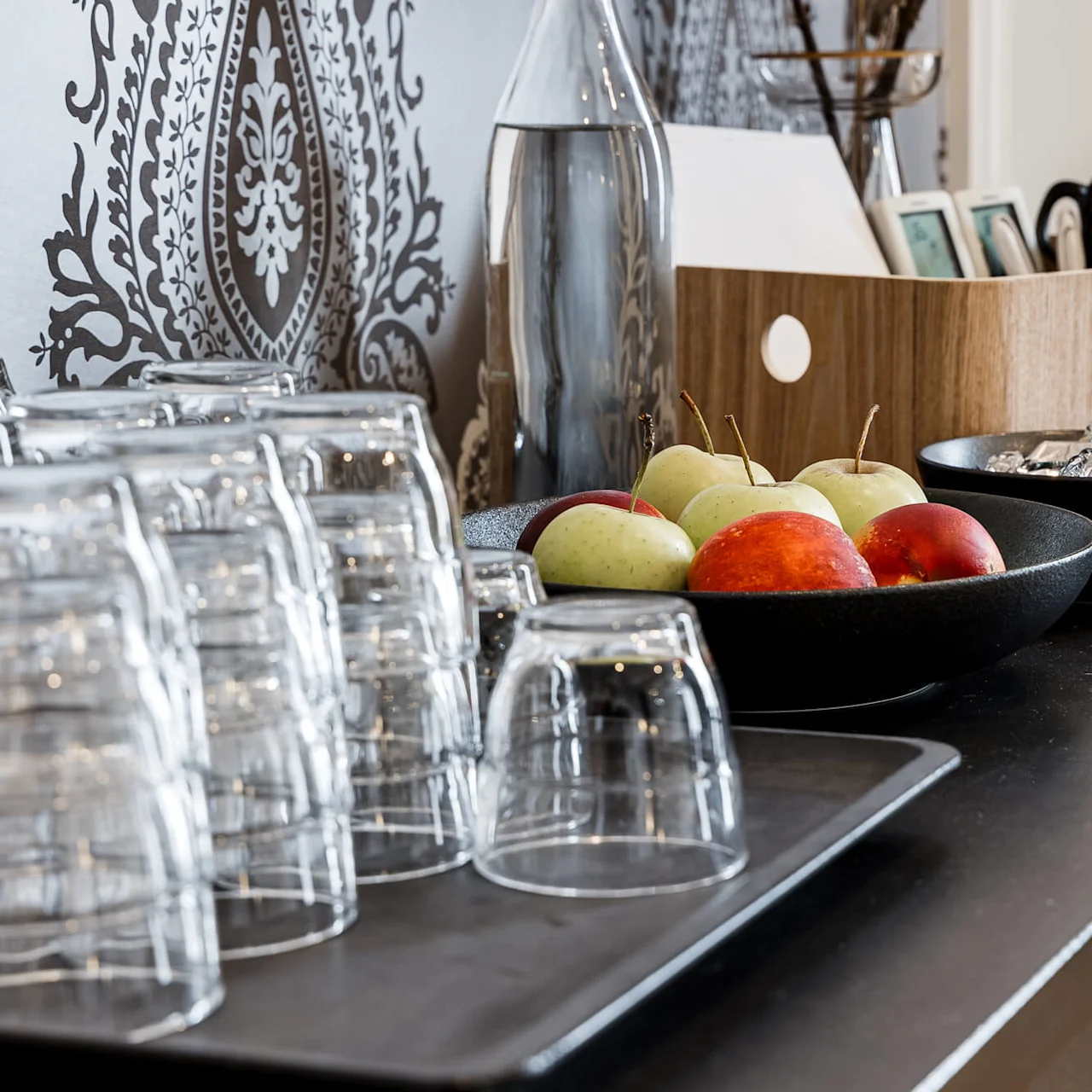 Apples in a bowl on a kitchen counter with glasses and decorative items, in a stylish home.