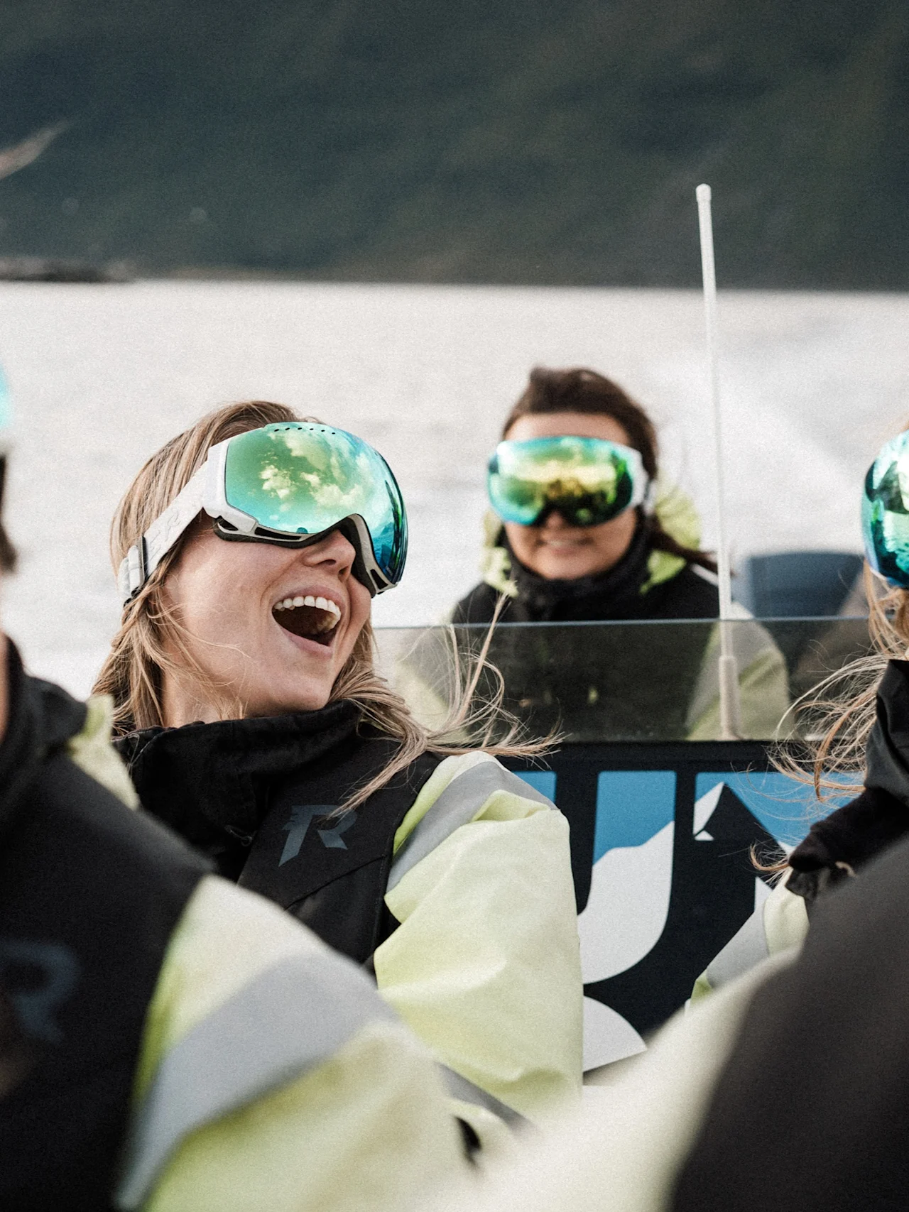 People in ski goggles laughing and enjoying an outdoor activity on the water, with reflections of the sky in their goggles.