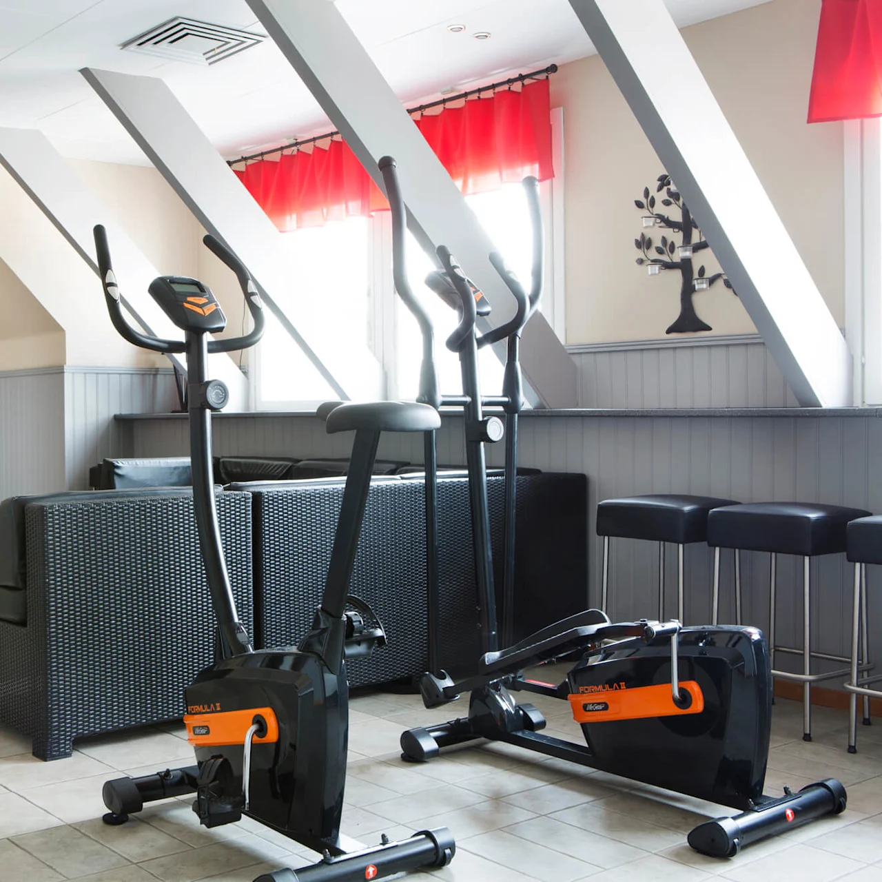 Exercise equipment in a well-lit room with windows, a TV, and a lounge area.