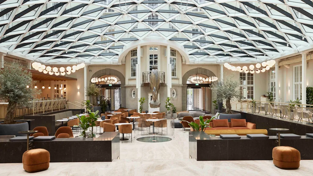 Gårdsplassens salongområde med glasstak på Villa Copenhagen. Et lyst, moderne rom med ulike sitteplasser, planter og en bar.