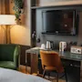Et velutstyrt hotellrom med et funksjonelt skrivebordsområde med TV, vannkoker og radio, supplert med innbydende lenestoler.