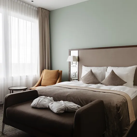 Ett mysigt hotellrum med en stor säng, en bekväm schäslong med badrockar och ett ljust fönster.