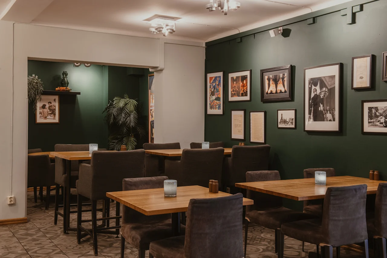 En mysig matplats på Home Hotel Grand, Helsingborg, med mörkgröna väggar prydda med inramad konst och träbord med levande ljus.