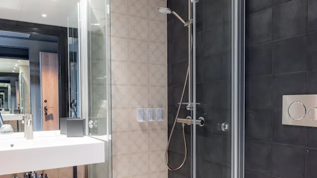 A modern bathroom with a shower, sink, and toilet, featuring contrasting light and dark tiles.