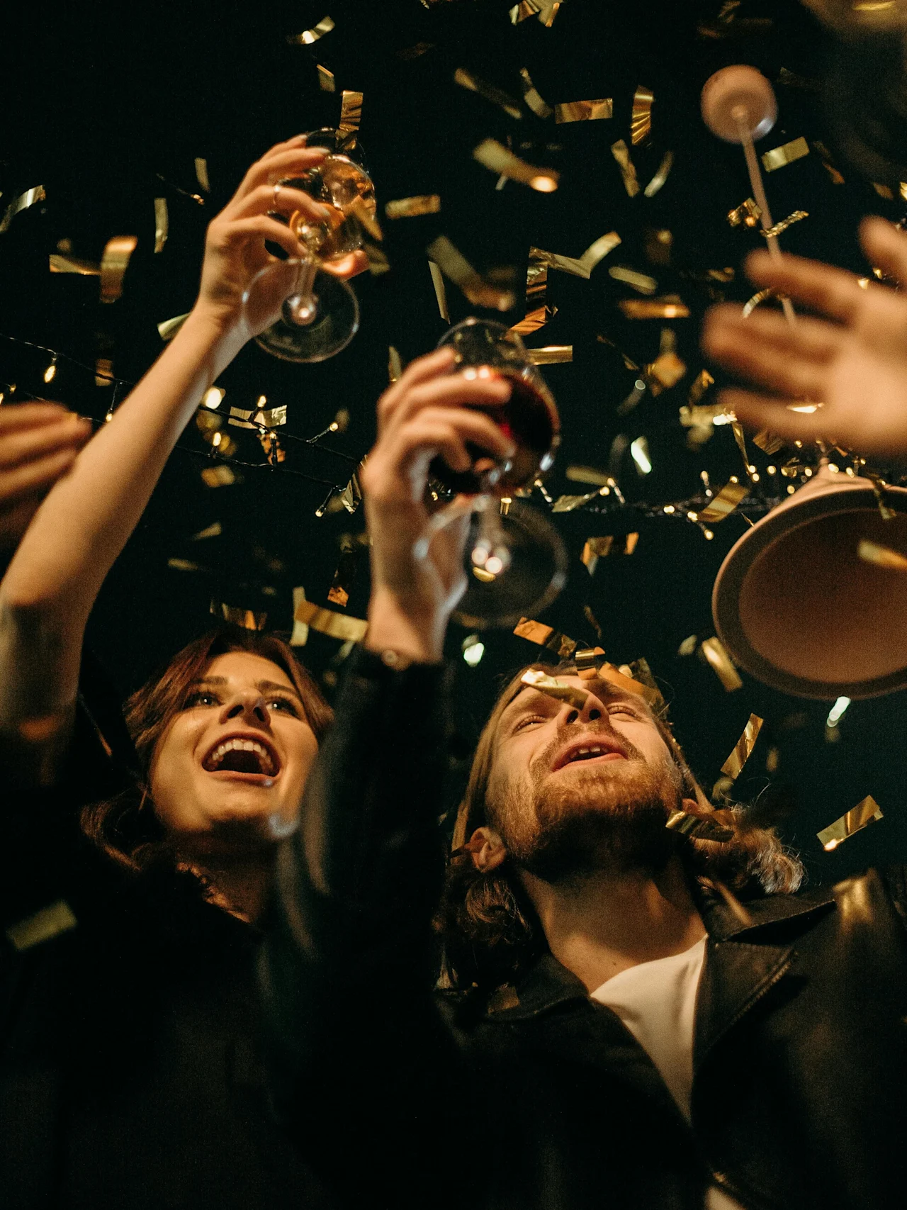 Människor höjer glasen i firande, omgivna av gyllene konfetti under dämpad belysning.