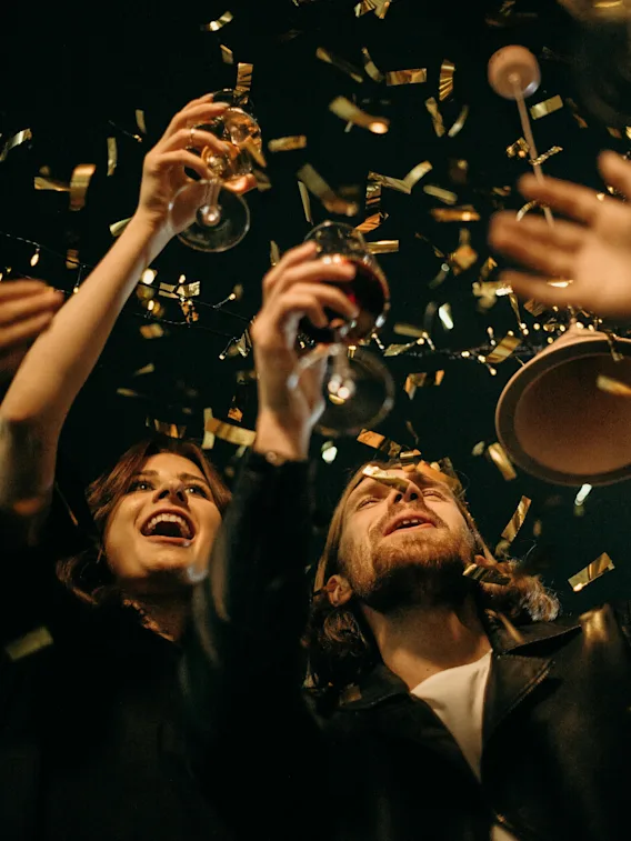 Människor höjer glasen i firande, omgivna av gyllene konfetti under dämpad belysning.