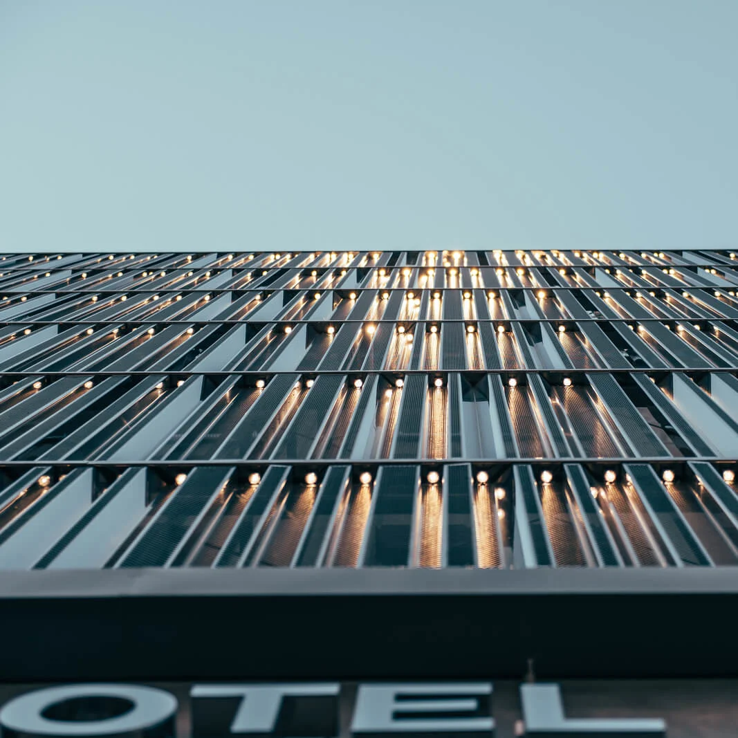 Building facade reflects light from aligned windows. A sign below reads, "HOTEL," with a clear sky overhead.