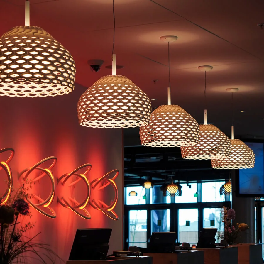Unika, mönstrade taklampor belyser en hotellreception i en modern, varmt upplyst interiör. Väggen visar dekorativa element. Text: "Clarion Hotel Energy."