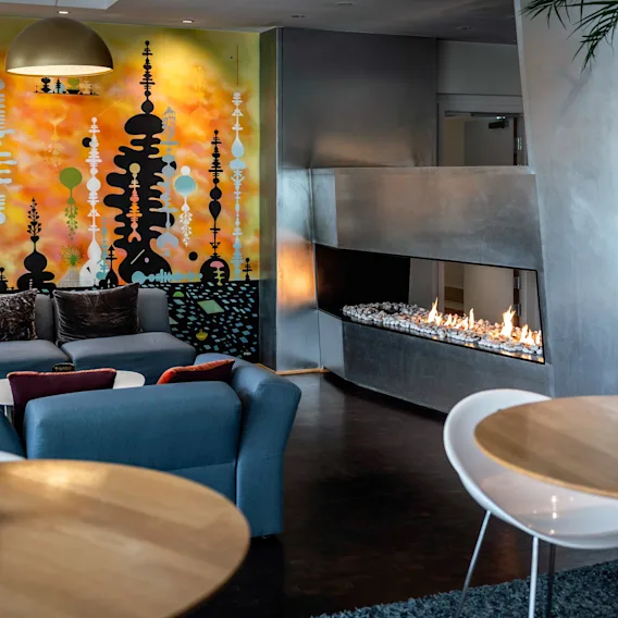 Et fargerikt veggmaleri dekorerer en moderne salong med blå sofaer og en elegant peis. Trebord og myk belysning skaper en koselig atmosfære.