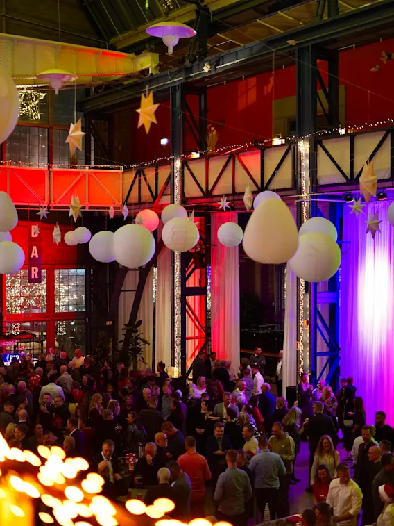 A lively crowd gathers at a festive indoor event decorated with hanging paper lanterns and warm lights.
