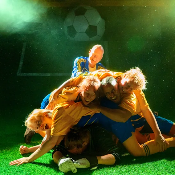 Fotbollsspelare som firar i en jublande hög på gräset under grönt ljus.