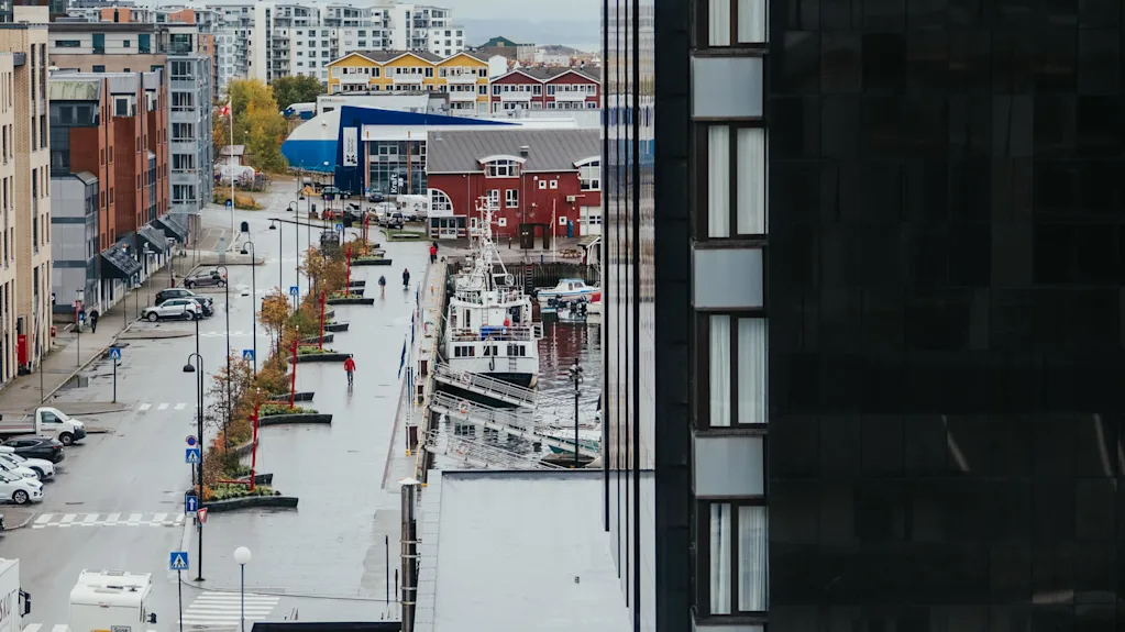 En gade linjer en havn med både fortøjet, omgivet af moderne og farverige bygninger i et urbant vandfrontsmiljø.