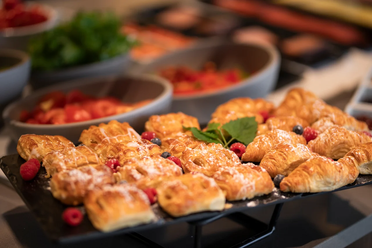En lækker morgenmadsbuffet med friskbagt bagværk, herunder croissanter og wienerbrød, pyntet med bær og flormelis.