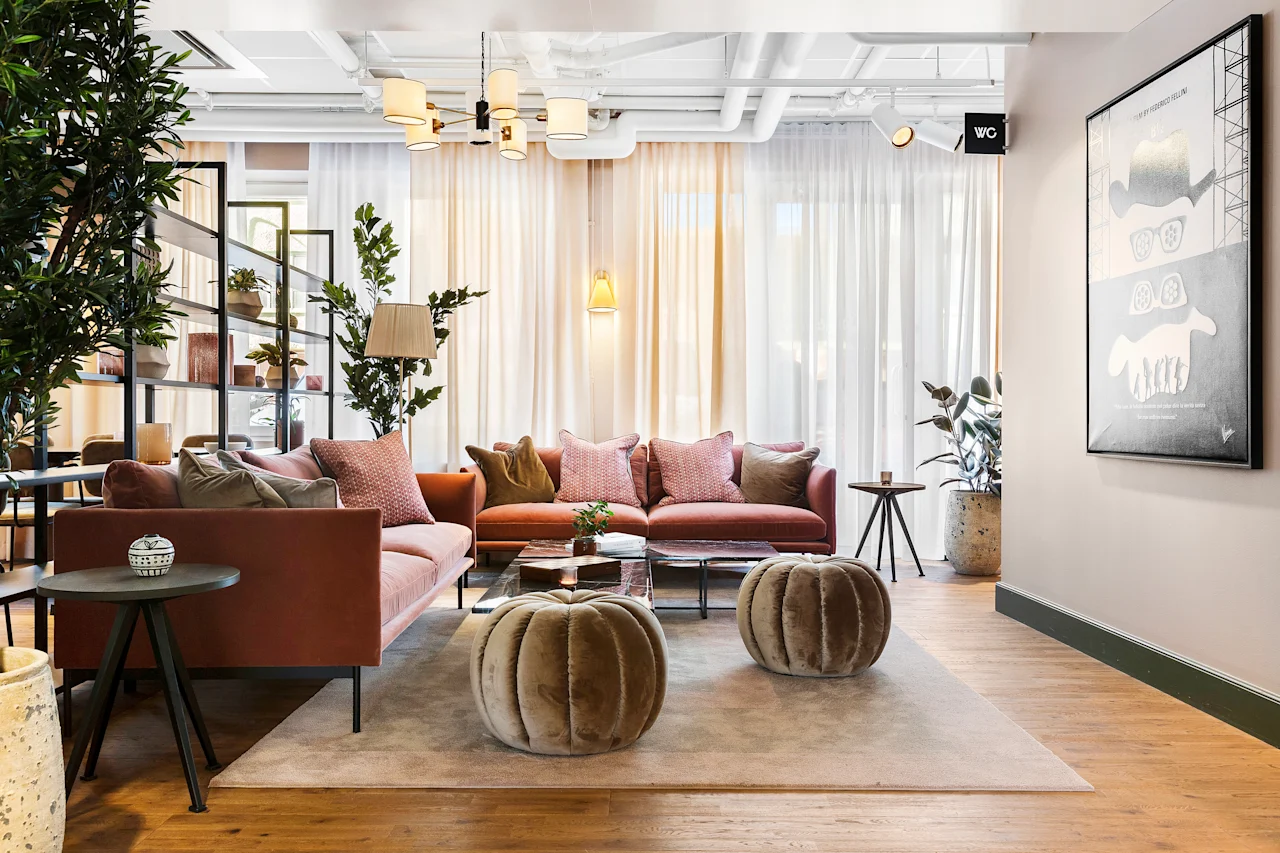 Moderne og koselig hotellobby med rosa sofaer, myke puffer og grønne planter under lunt lys.