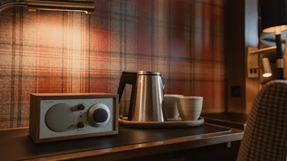 Et hyggeligt skrivebordsarrangement med en radio med Bluetooth, en kedel og to kopper på en bakke, oplyst af en varm lampe.