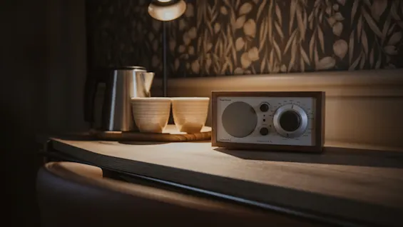 Lämmin ja kutsuva näkymä radiolla, vedenkeittimellä ja kupeilla puupinnalla, lampun valossa. Radio: Audio Model One.