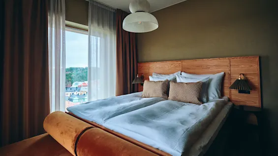 Et koselig hotellrom med en stor seng og et vindu som tilbyr en naturskjønn utsikt over en by og grønne åser.