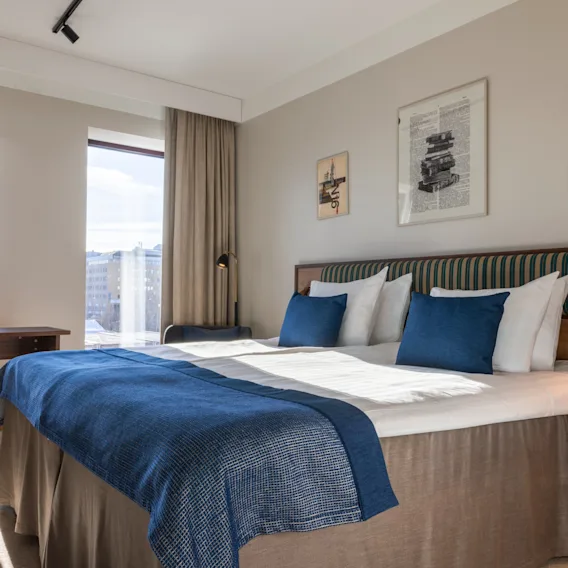 A bright hotel room with a comfortable bed, a desk by the window, and artwork on the wall.
