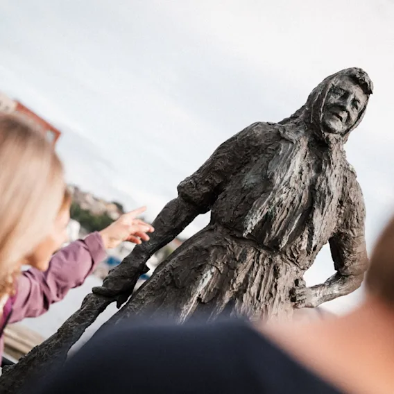 En turist som peker mot bronsestatuen Klippfiskkjerringa i Kristiansund.