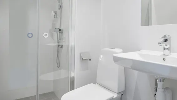 Duschkabin med glasdörr bredvid en vit toalett och handfat i ett rent, ljust badrum.