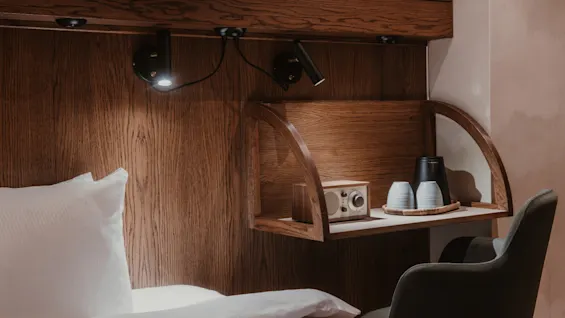 Home Hotel Baltzar - Compact Cabin. A cozy hotel room with a wooden headboard, reading lights, a small shelf with a radio, kettle, and cups.