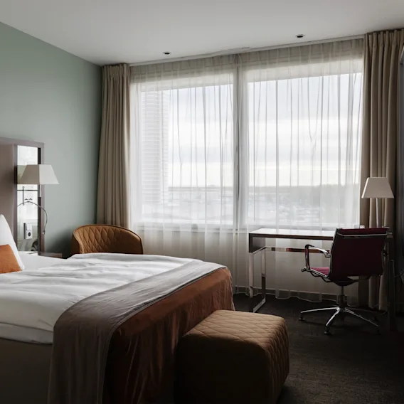 Ett lugnt hotellrum med en bekväm säng, ett skrivbord för produktivitet och stora fönster som ger en ljus atmosfär.