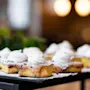 Delicious square cakes topped with whipped cream, powdered sugar, and sprinkles, arranged on a tray with a warm, blurred background.