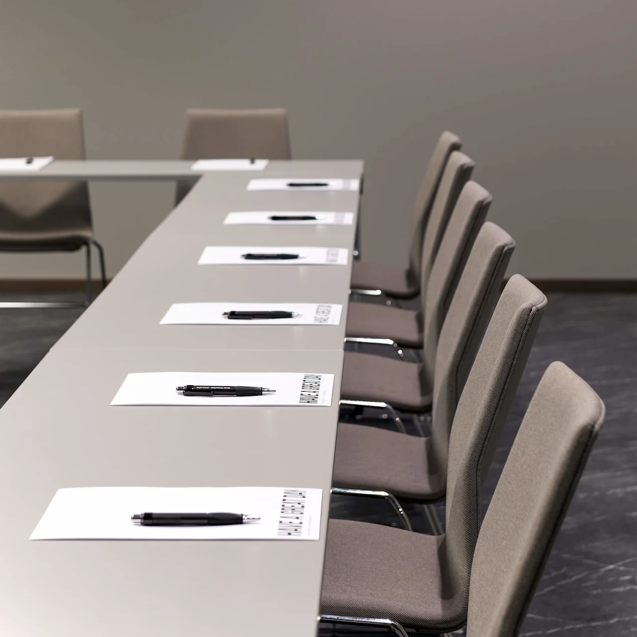 Møteromsbord med stoler, papirer og penner. Papirene merket "ENTHUSIASM." Stolene er pent alignert, og skaper en organisert atmosfære egnet for møter eller presentasjoner.