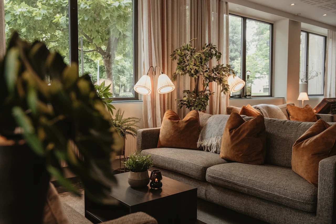 A cozy lounge area with comfortable sofas, warm lighting, and large windows looking out onto lush greenery.