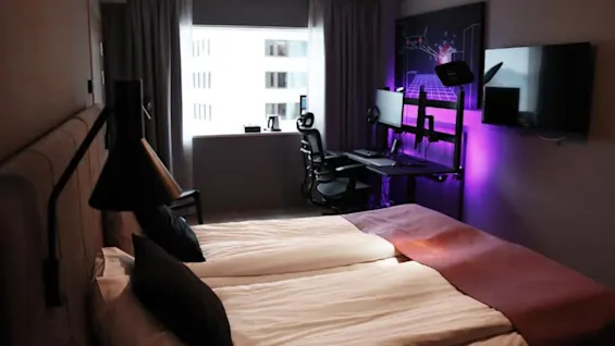 Quality Hotel Match værelse med en hyggelig seng og et levende gaming setup med dobbelte skærme og lilla stemningsbelysning.