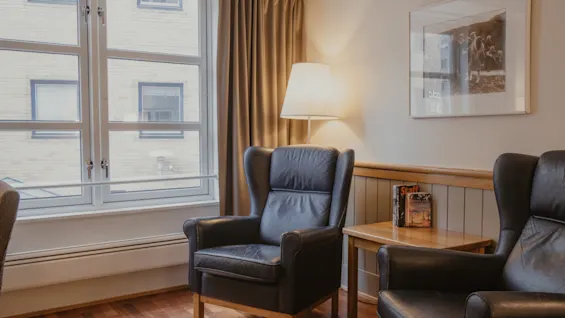 A cozy seating area with two comfortable armchairs, a side table with books, and a lamp next to a large window.