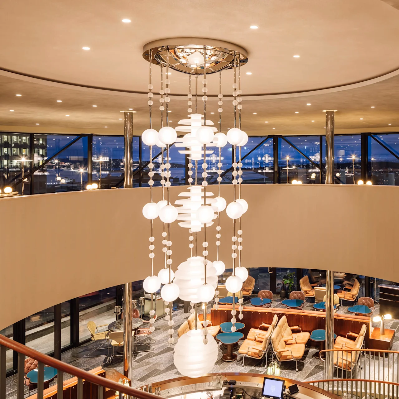 En moderne lounge med cirkulære lysekroner, komfortable siddepladser og store vinduer med udsigt til natten.