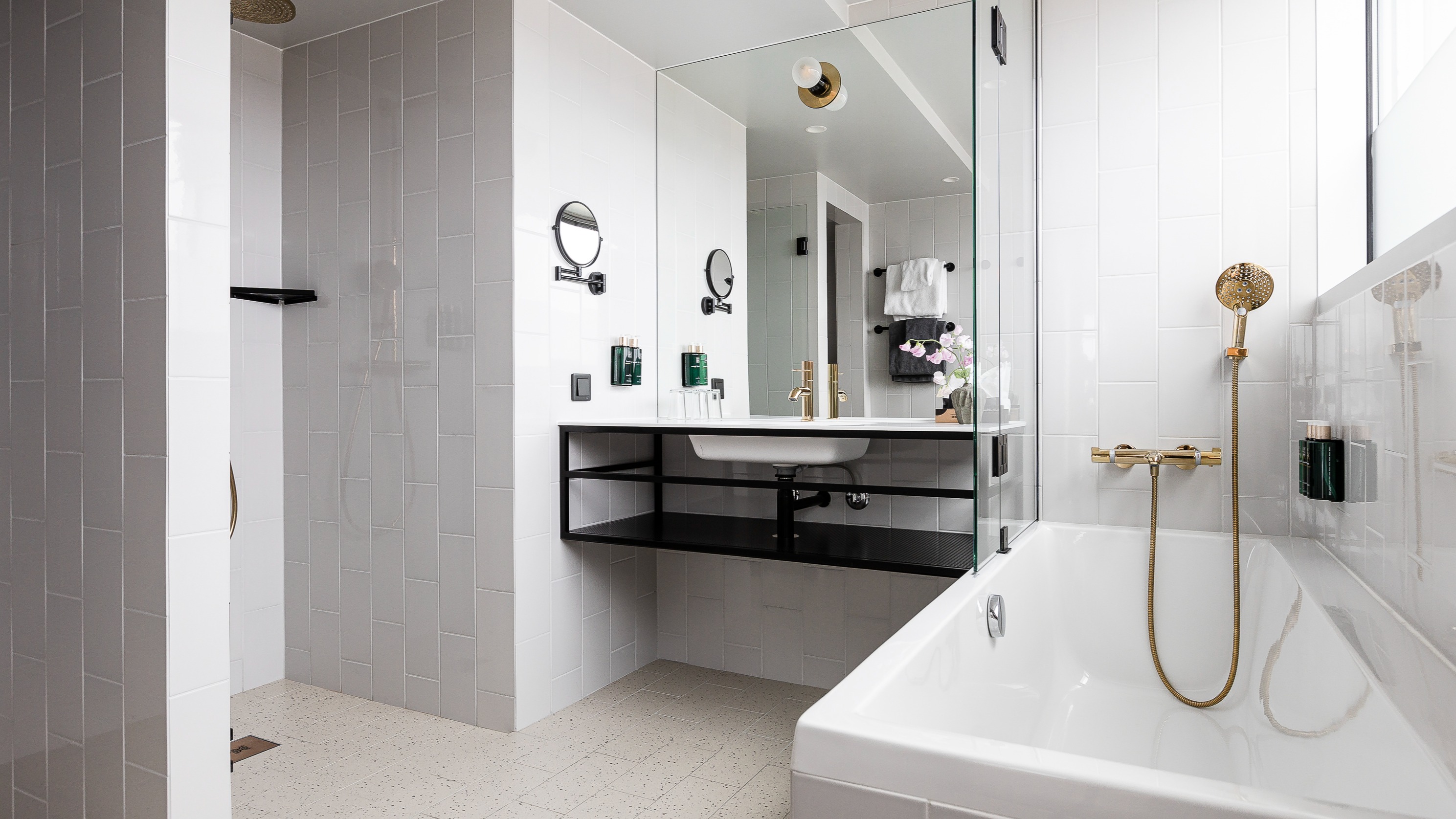 Et moderne badeværelse med bruser, håndvask med spejl og badekar med gyldent brusehoved.