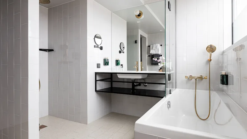 Et moderne badeværelse med bruser, håndvask med spejl og badekar med gyldent brusehoved.