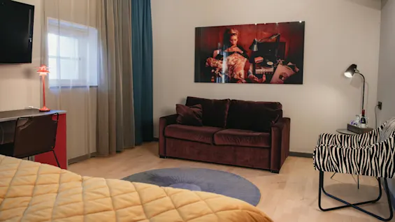 En brun soffa står mot en vägg, prydd med ett stort foto, bredvid en zebramönstrad stol och ett litet bord med lampa i ett mysigt rum.