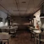 A dimly lit restaurant dining area with multiple tables and chairs, decorated with small plants and framed art on the walls.