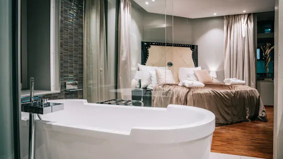 Ett lyxigt hotellrum med ett fristående badkar och en bekväm säng, åtskilda av en glasvägg.