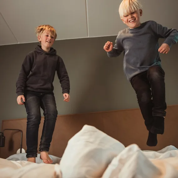 To glade barn har det gøy med å hoppe på en seng på et hotellrom.