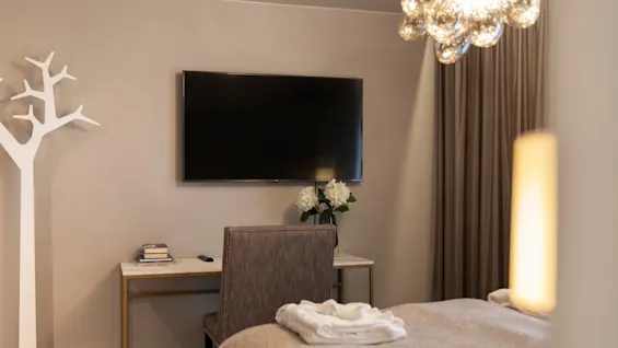 A cozy hotel room at Home Hotel Grand Bodø with a bed, desk, TV, and a stylish chandelier, ready for a comfortable stay.