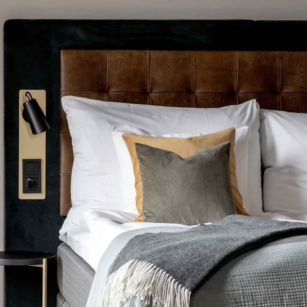 Viihtyisä ja moderni hotellisänky Clarion Hotel Sundsvallissa, jossa on ruskea tuftattu sängynpääty, pehmeät tyynyt ja lämpimät peitot.