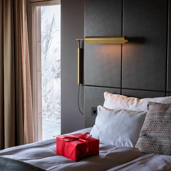 En rød gaveeske på et hvitt oppredd hotellrom med utsyn til et snødekt vindu.