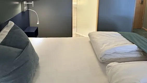Viihtyisä hotellihuone kahdella siististi pedatulla sängyllä, valmiina mukavaan oleskeluun.
