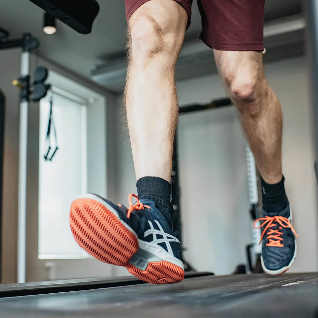 Person running on a treadmill, focus on the legs and feet, in a gym.