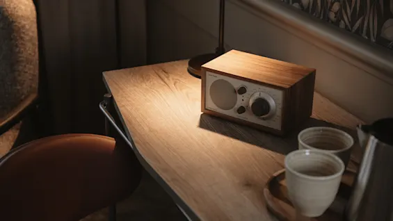 A cozy scene with a wooden radio and a lamp on a desk, accompanied by a tray with cups and a kettle. Model One.