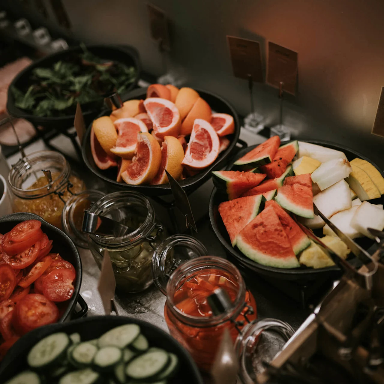 Forskellige friske frugter og grøntsager udstillet i skåle og krukker på et buffetbord.