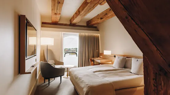 Ett mysigt hotellrum med en stor säng, TV, sittgrupp och skrivbord, med synliga träbjälkar.