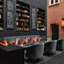 En hyggelig lounge med en moderne pejs, komfortable siddepladser og bogreoler. Et TV viser en pejs, med tavler der siger enjoy og cheers.