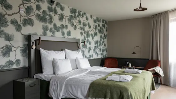 Kutsuva hotellihuone, jossa on mukava sänky vihreällä peitolla, männynoksatapetti ja oleskelualue.