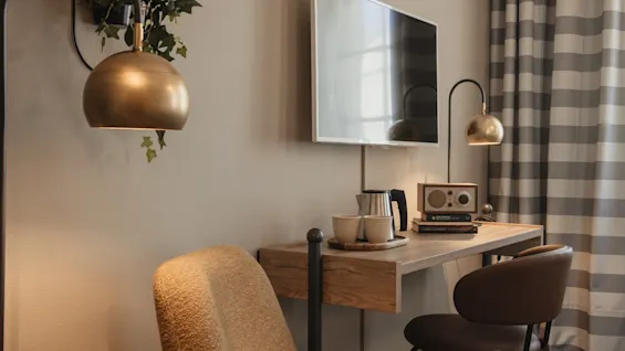 A cozy room with a desk, TV, and comfortable seating, featuring a kettle, cups, and a radio for a relaxing stay.