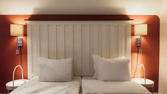 Ett mysigt hotellrum på Home Hotel Grand, Helsingborg, med två bekväma sängar, en vit sänggavel och varm väggbelysning.